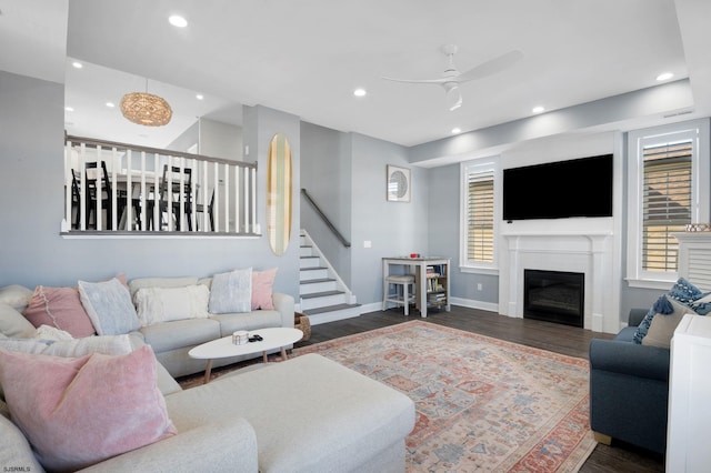 living room with baseboards, a glass covered fireplace, stairway, wood finished floors, and recessed lighting