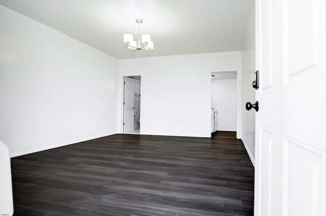 spare room with dark wood-style floors, baseboards, and an inviting chandelier