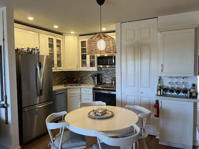 kitchen with decorative light fixtures, stainless steel appliances, tasteful backsplash, glass insert cabinets, and white cabinetry