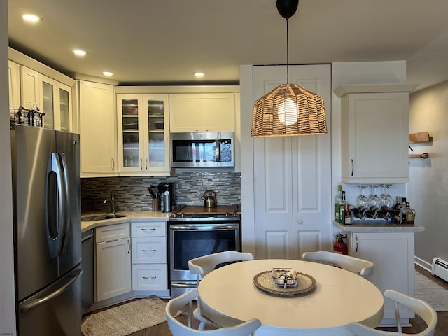 kitchen with stainless steel appliances, a sink, light countertops, decorative backsplash, and glass insert cabinets