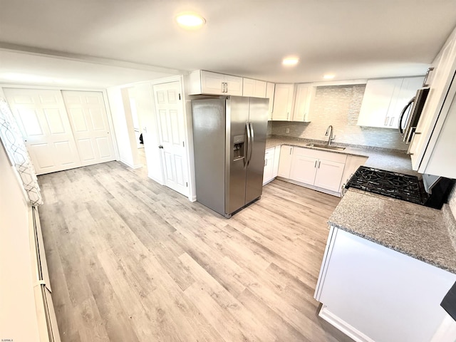 kitchen featuring light wood finished floors, stainless steel fridge, a sink, and stone countertops