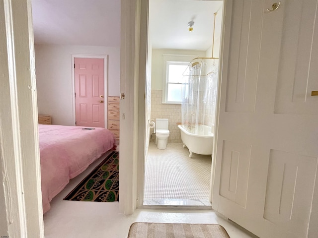 bathroom with toilet, a wainscoted wall, tile patterned flooring, shower / bath combination with curtain, and tile walls