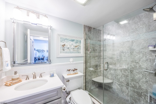 full bathroom with a stall shower, wainscoting, vanity, and toilet