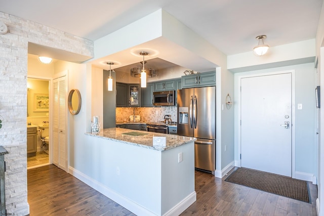 kitchen with light stone counters, stainless steel appliances, dark wood-type flooring, a peninsula, and decorative backsplash