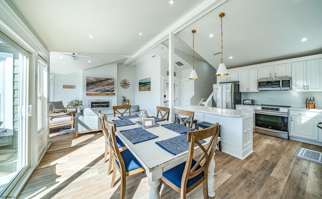 dining area featuring lofted ceiling, light wood-style flooring, recessed lighting, a large fireplace, and stairs