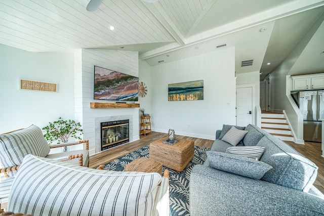 living room with baseboards, lofted ceiling with beams, wood finished floors, stairs, and a fireplace