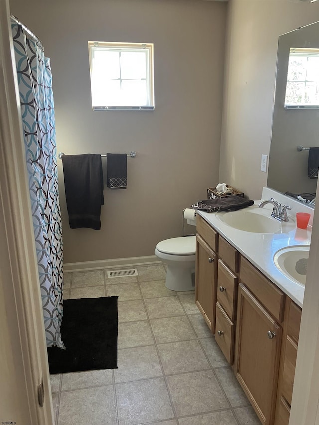 full bath with toilet, a sink, double vanity, and visible vents