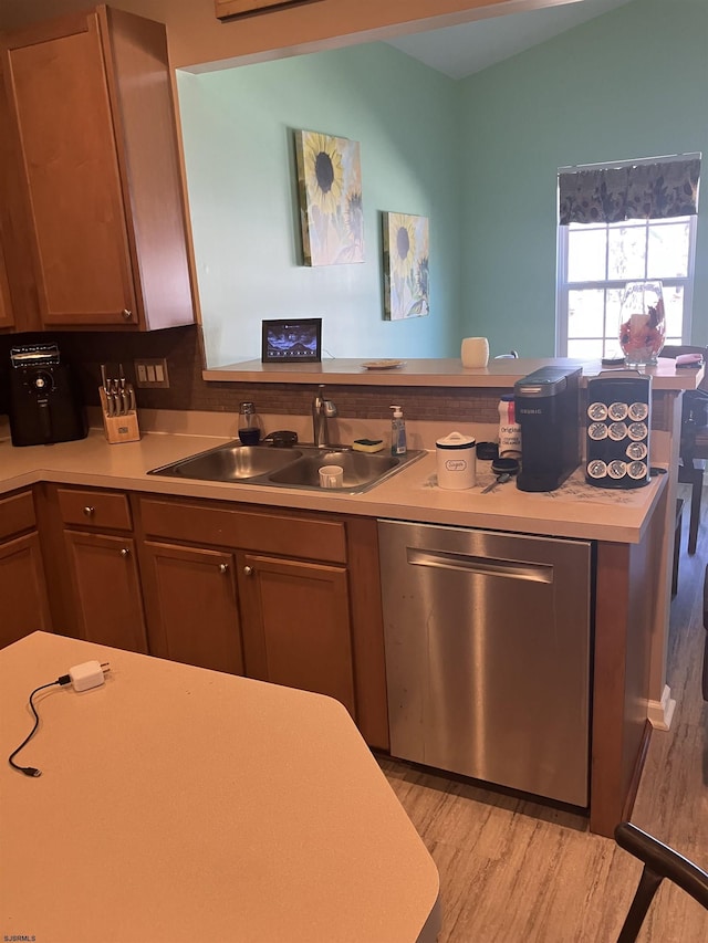 kitchen with light countertops, a sink, light wood finished floors, dishwasher, and a peninsula