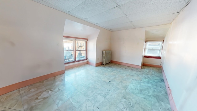 empty room with a paneled ceiling, radiator, and baseboards