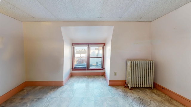 spare room featuring baseboards, a drop ceiling, and radiator