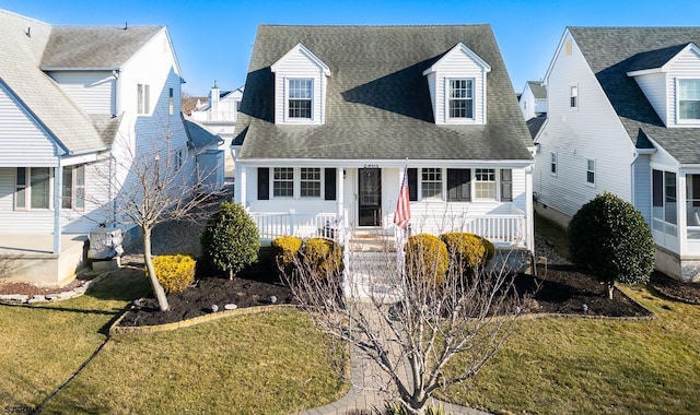 new england style home featuring covered porch, a shingled roof, and a front lawn