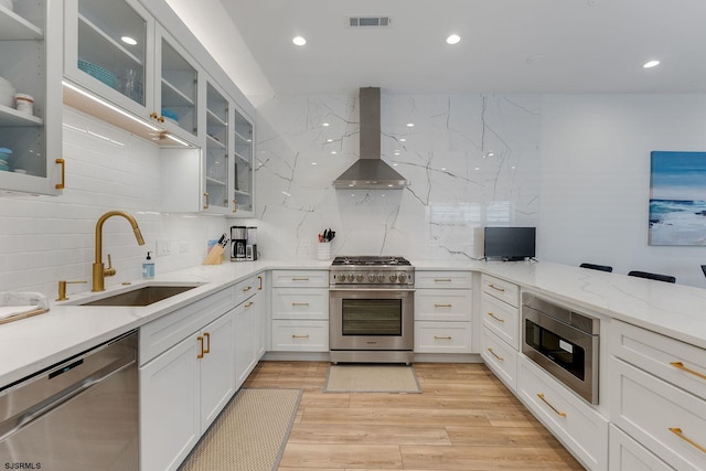 kitchen with visible vents, wall chimney exhaust hood, stainless steel appliances, light wood-type flooring, and a sink