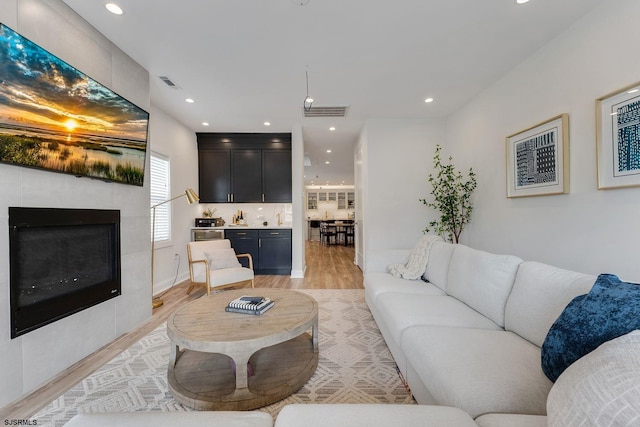 living area featuring a tile fireplace, visible vents, light wood-style flooring, and recessed lighting