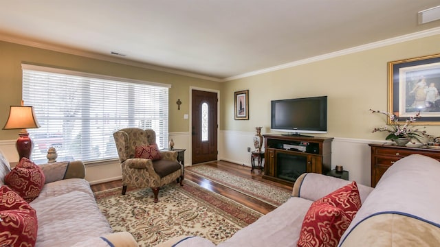 living area featuring crown molding, a fireplace, visible vents, wainscoting, and wood finished floors