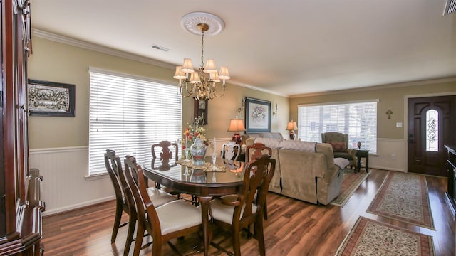 dining space featuring a wainscoted wall, visible vents, an inviting chandelier, dark wood finished floors, and crown molding