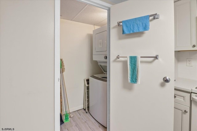 laundry room with stacked washer / drying machine, laundry area, light wood-style flooring, and baseboards