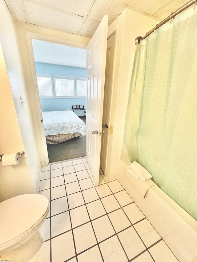 ensuite bathroom featuring a drop ceiling, ensuite bath, toilet, and tile patterned floors