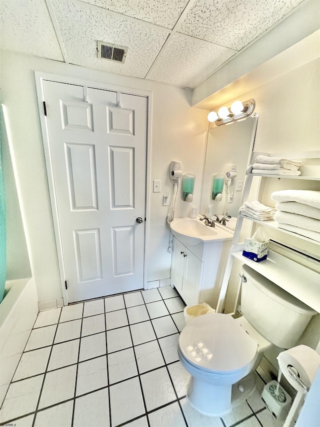 full bathroom with visible vents, toilet, vanity, a drop ceiling, and tile patterned floors