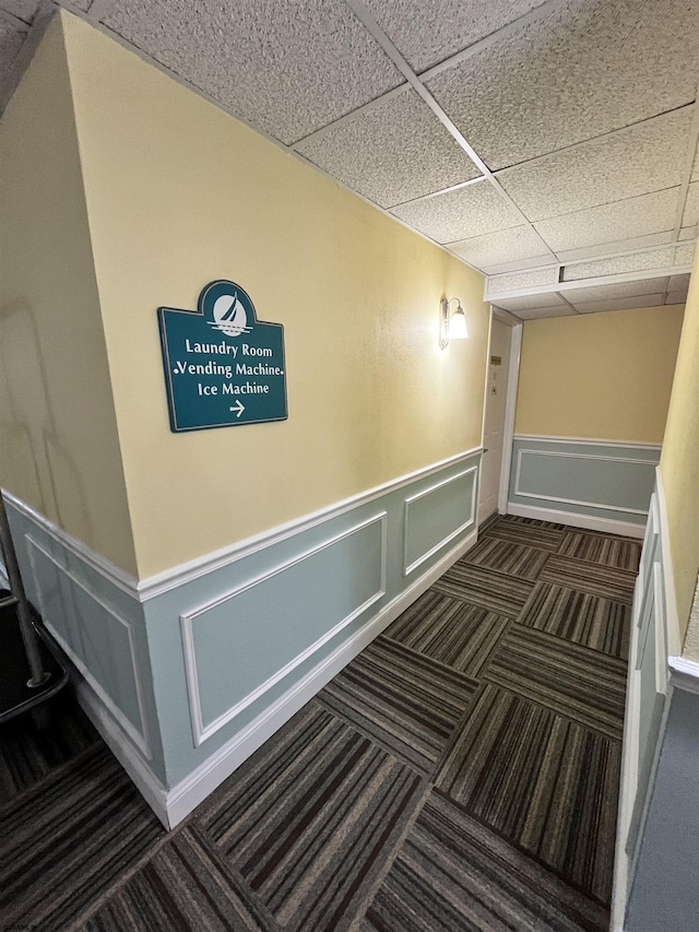 hallway featuring a paneled ceiling, a wainscoted wall, and carpet flooring