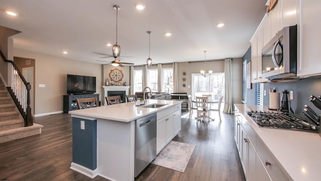 kitchen with stainless steel appliances, a sink, white cabinetry, light countertops, and a center island with sink