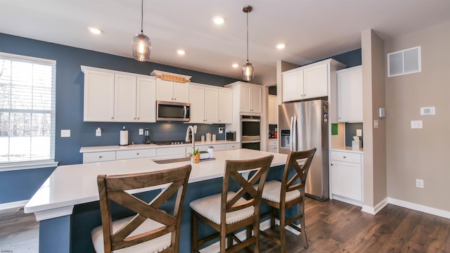 kitchen featuring stainless steel appliances, a sink, visible vents, light countertops, and an island with sink