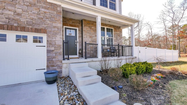 view of exterior entry with stone siding, a porch, an attached garage, and fence