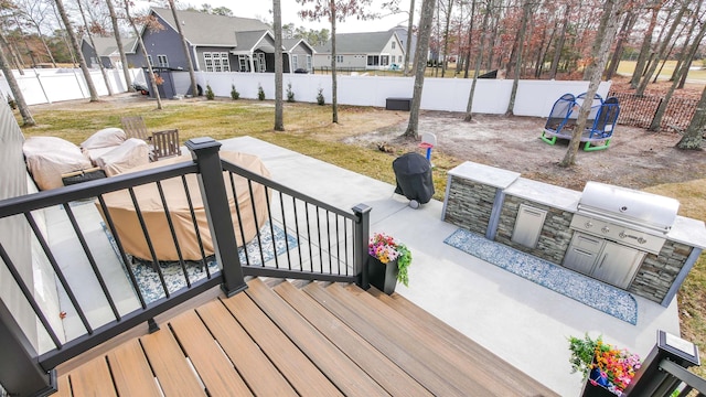 deck featuring a trampoline, a residential view, a fenced backyard, and exterior kitchen