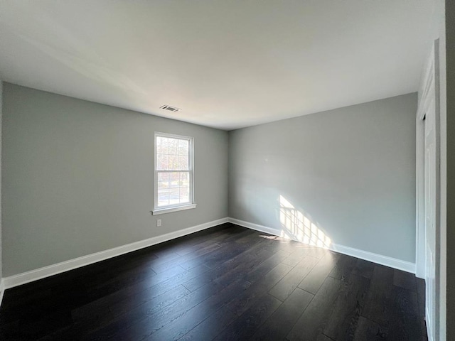 spare room with dark wood-style floors, visible vents, and baseboards