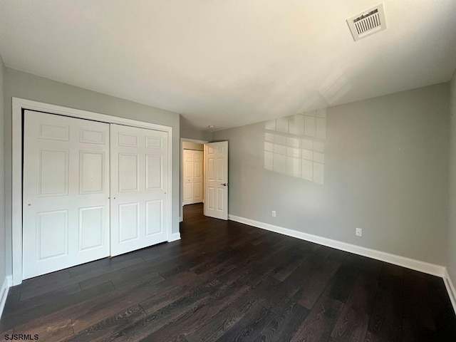 unfurnished bedroom featuring baseboards, visible vents, dark wood finished floors, lofted ceiling, and a closet