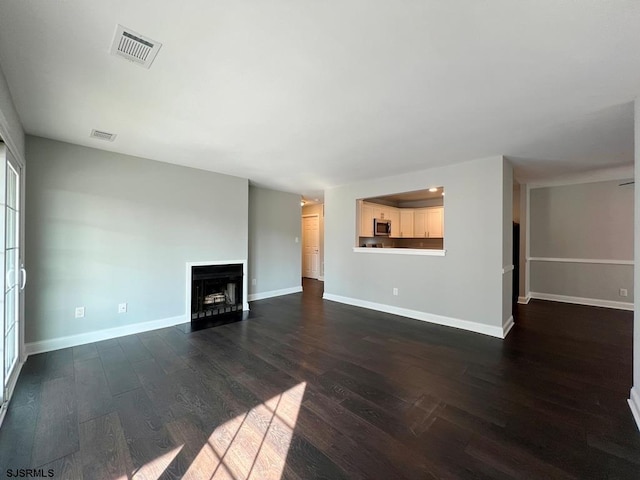 unfurnished living room with a fireplace with flush hearth, visible vents, dark wood finished floors, and baseboards