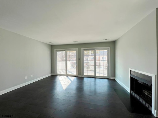 unfurnished living room with dark wood-type flooring, a fireplace with flush hearth, visible vents, and baseboards