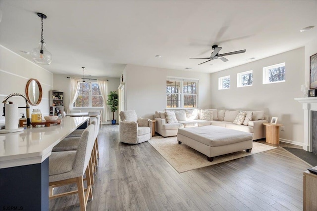 living room featuring a fireplace with flush hearth, ceiling fan, and wood finished floors