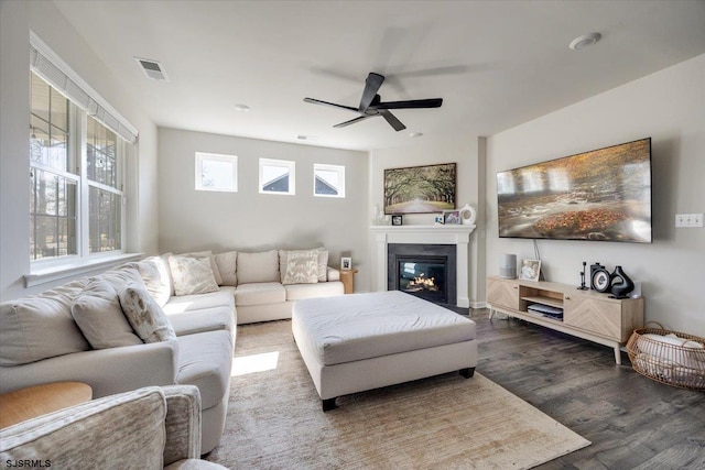 living room featuring a ceiling fan, a glass covered fireplace, visible vents, and wood finished floors