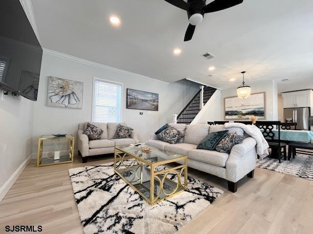 living area with visible vents, baseboards, light wood-style floors, stairway, and crown molding