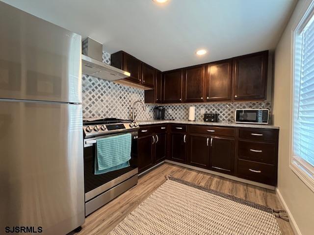 kitchen with dark brown cabinetry, stainless steel appliances, light wood-style floors, light countertops, and decorative backsplash