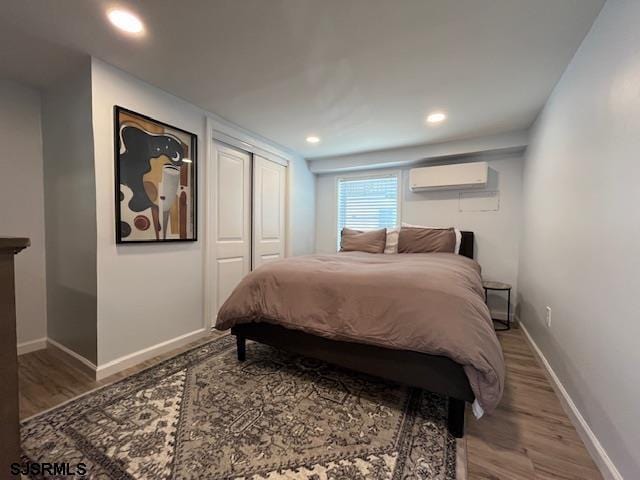 bedroom featuring a closet, an AC wall unit, baseboards, and wood finished floors