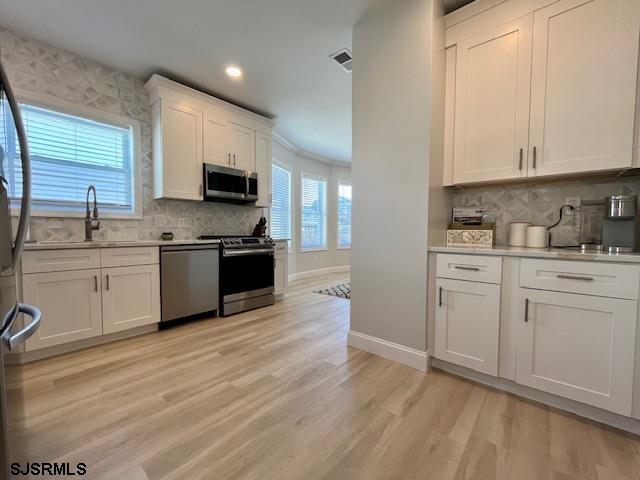 kitchen featuring stainless steel appliances, a sink, visible vents, baseboards, and white cabinetry