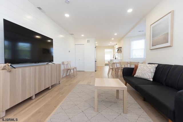 living room featuring light wood-type flooring, visible vents, wooden walls, and recessed lighting