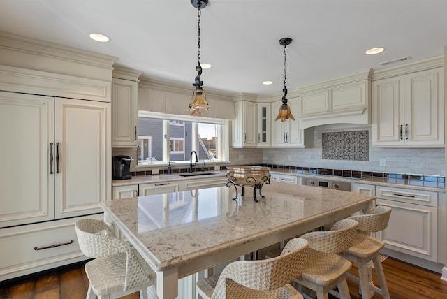 kitchen with visible vents, a breakfast bar area, light stone counters, custom exhaust hood, and a sink