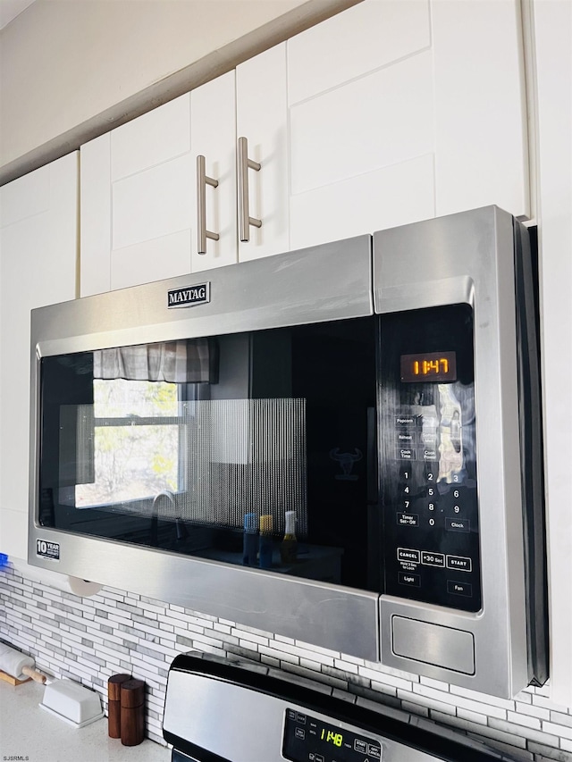 details featuring stainless steel microwave, decorative backsplash, and white cabinets