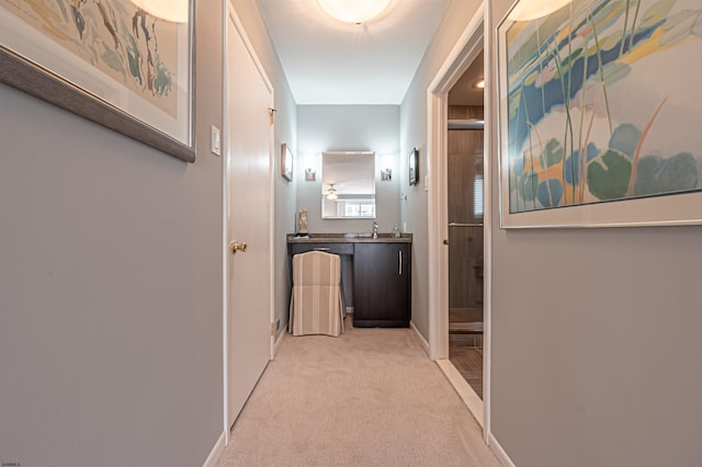 corridor featuring light carpet, a sink, and baseboards