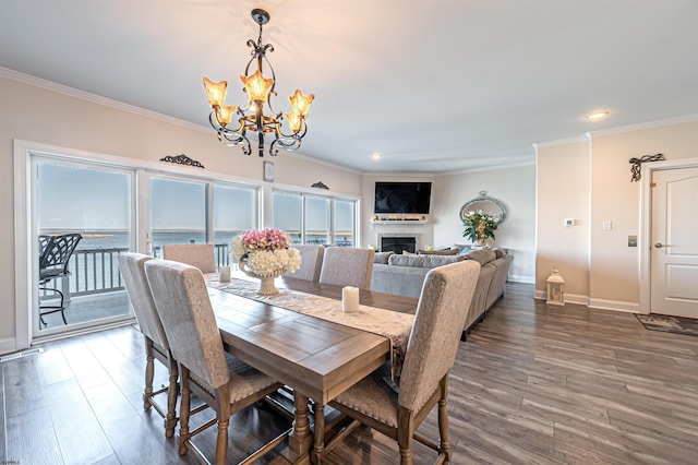 dining space with baseboards, wood finished floors, crown molding, a fireplace, and a notable chandelier