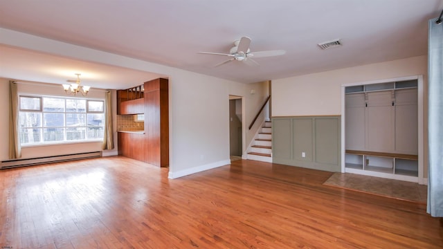 unfurnished living room featuring visible vents, stairway, wood finished floors, a baseboard heating unit, and ceiling fan with notable chandelier