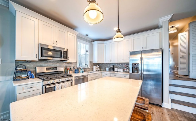 kitchen featuring stainless steel appliances, wood finished floors, a kitchen island, a sink, and tasteful backsplash