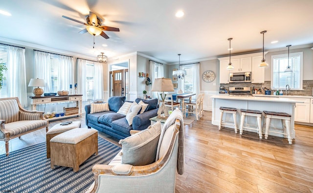 living area featuring recessed lighting, light wood-style flooring, crown molding, and ceiling fan with notable chandelier