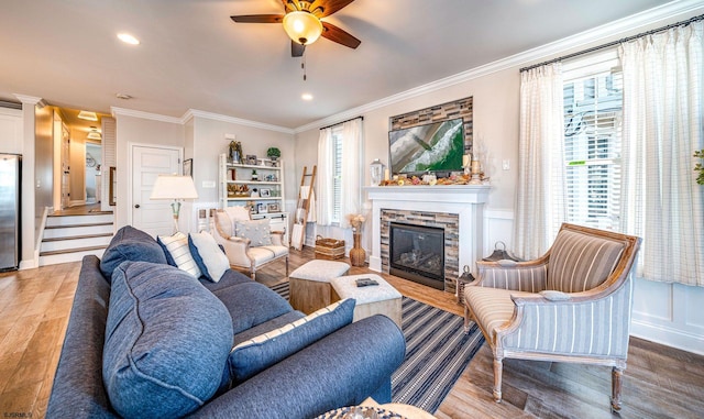 living room with a stone fireplace, a decorative wall, crown molding, and wood finished floors