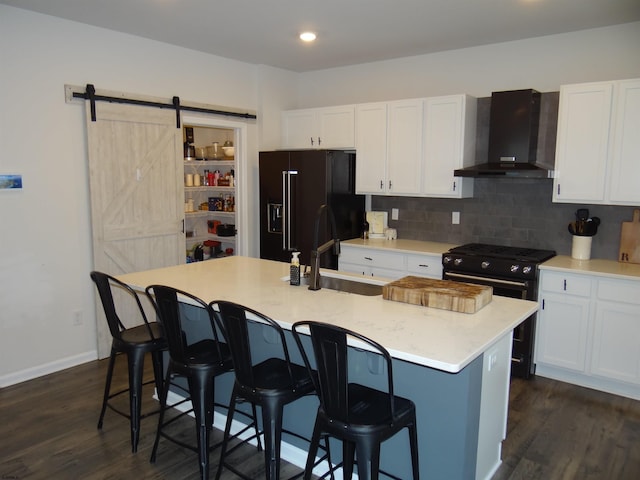 kitchen featuring wall chimney exhaust hood, black appliances, a barn door, and white cabinets