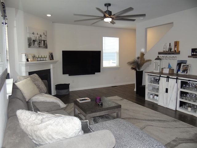 living room featuring a fireplace, ceiling fan, a bar, wood finished floors, and baseboards