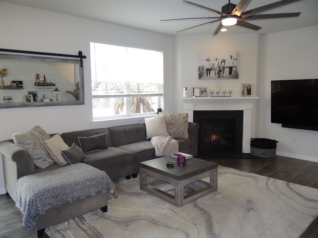 living area featuring a fireplace with flush hearth, baseboards, ceiling fan, and wood finished floors