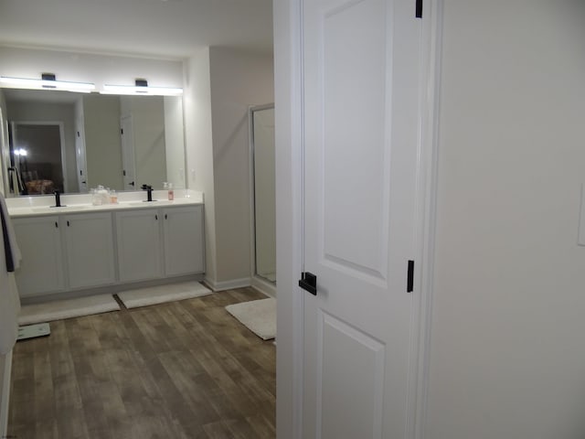 bathroom with double vanity, a shower stall, a sink, and wood finished floors